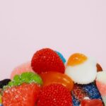 Colorful assorted gummy candies piled together on a pink background, including strawberry, blue raspberry, and fried egg shap