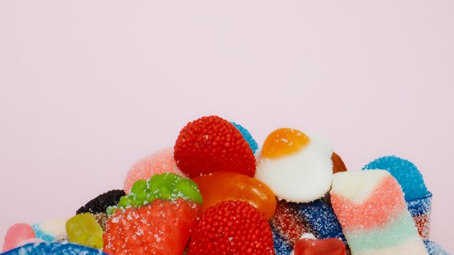 Colorful assorted gummy candies piled together on a pink background, including strawberry, blue raspberry, and fried egg shap